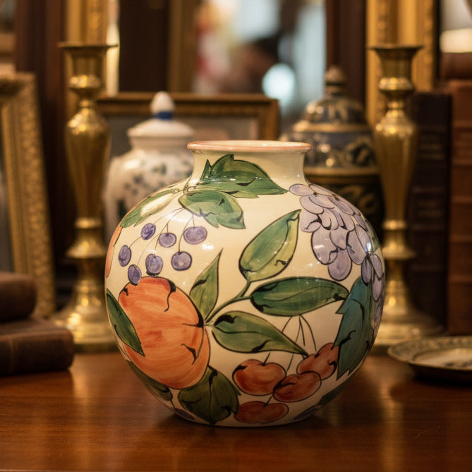 Decorative ceramic vase with floral and fruit design on a wooden surface.